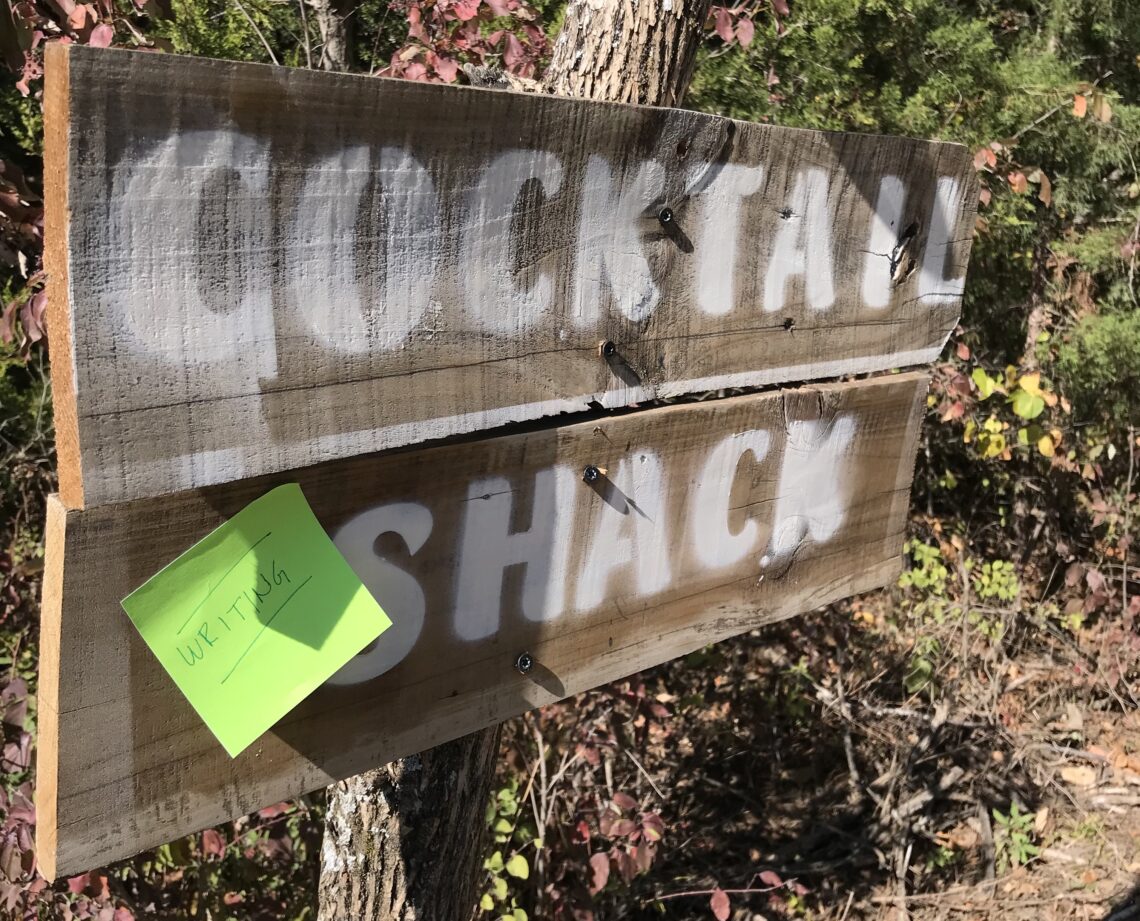 Wooden sign reading "cocktail shack" with sticky note reading "writing shack"