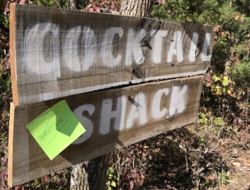 Wooden sign reading "cocktail shack" with sticky note reading "writing shack"